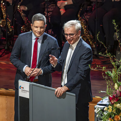 Bild vergr&ouml;&szlig;ern: Zwei M&auml;nner in Anzug stehen am Rednerpult.