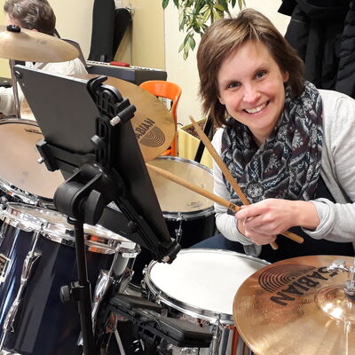 Bild vergrößern: Katharina Reinholz lächelnd mit Schal während sie die Drums spielt.
